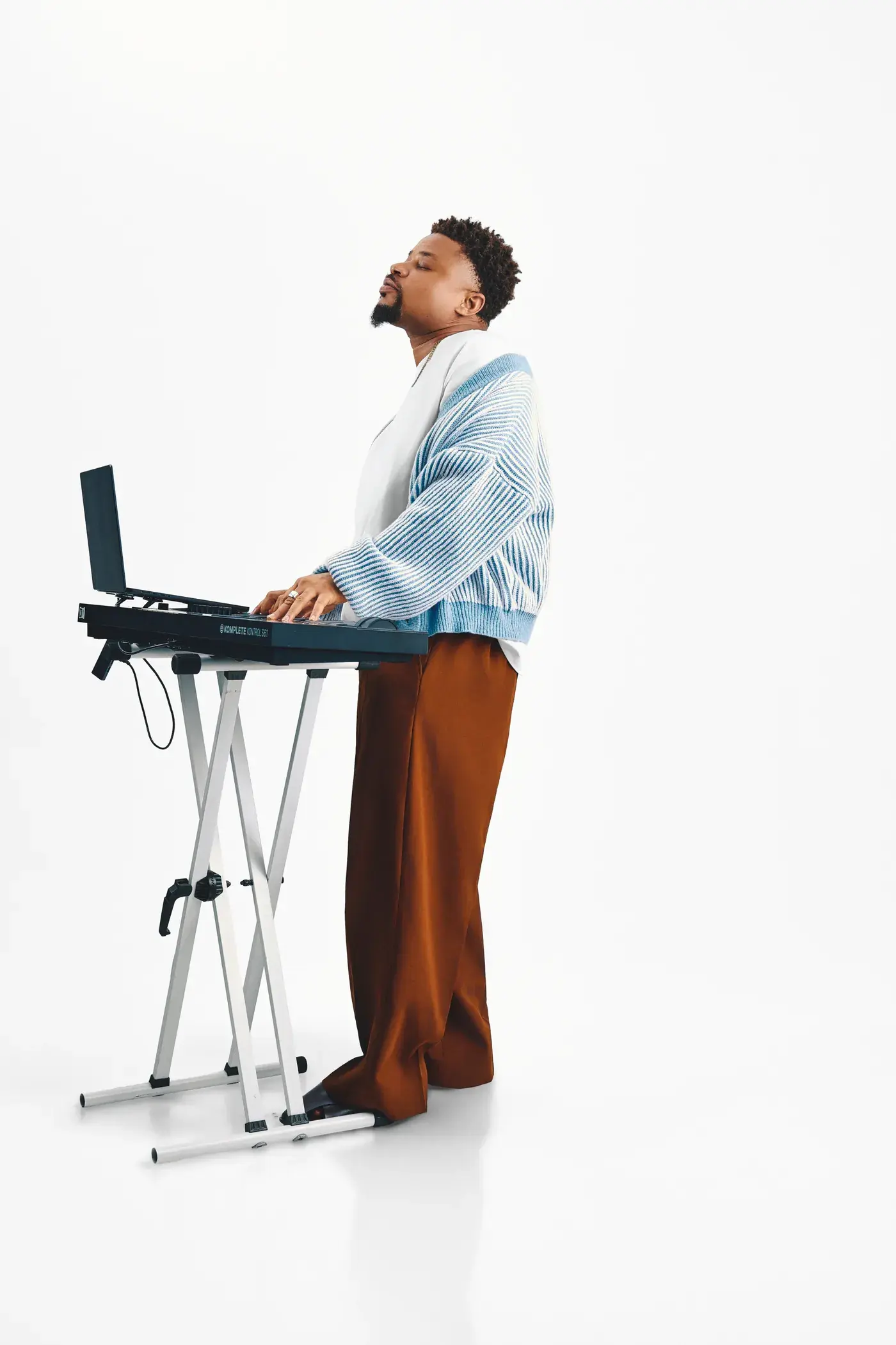 Ko'rale at the keys, head raised and eyes closed, in a blue cardigan on white