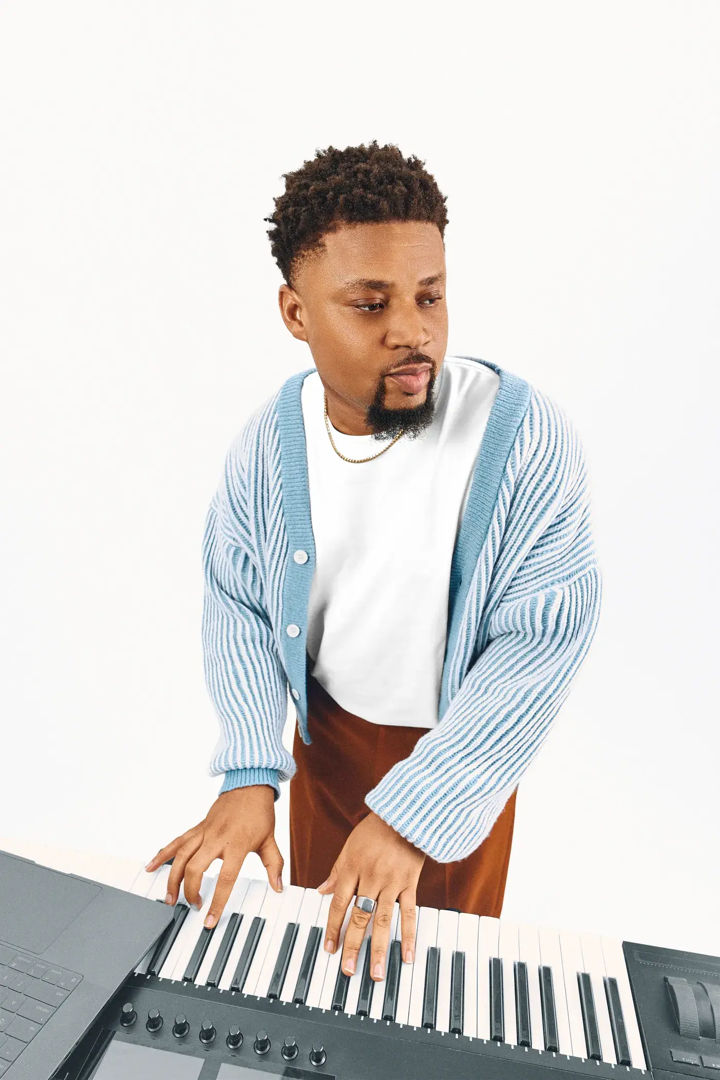 Ko'rale looking down at the keys in a blue cardigan, white backdrop