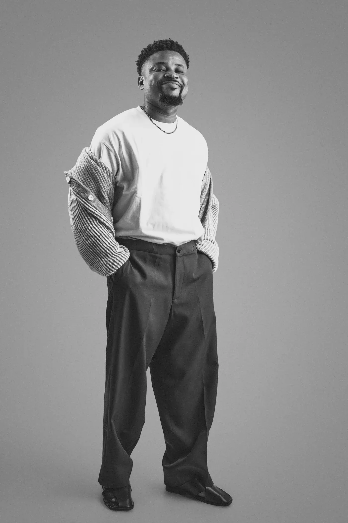Black and white full-length photograph of Ko'rale smiling with his hands in his pockets