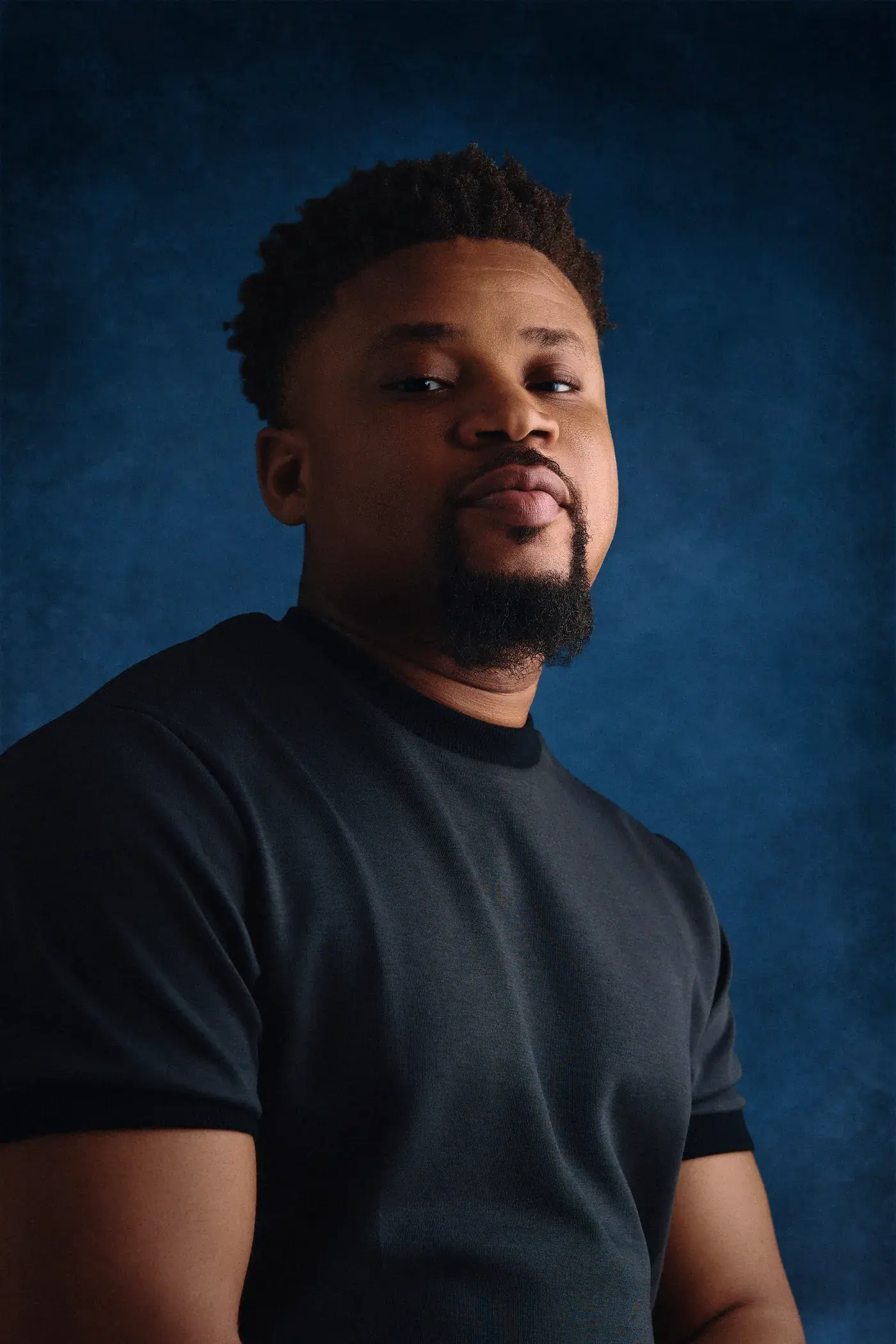Ko'rale in a black tee against a deep blue studio backdrop