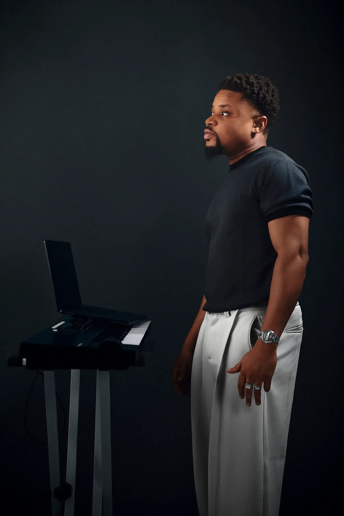 Ko'rale in profile at a laptop and keyboard against a charcoal backdrop