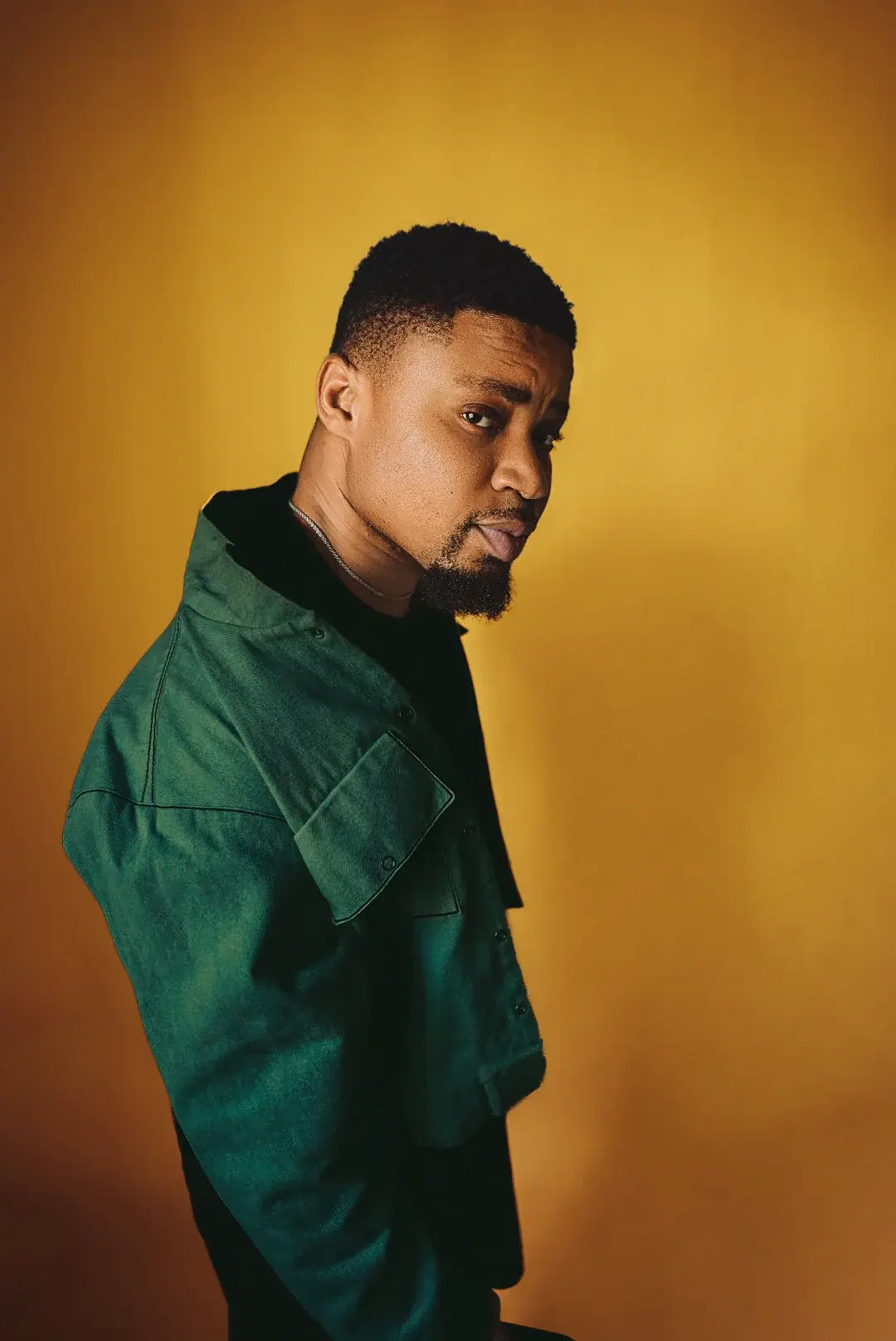 Ko'rale in a green jacket in profile against a gold backdrop