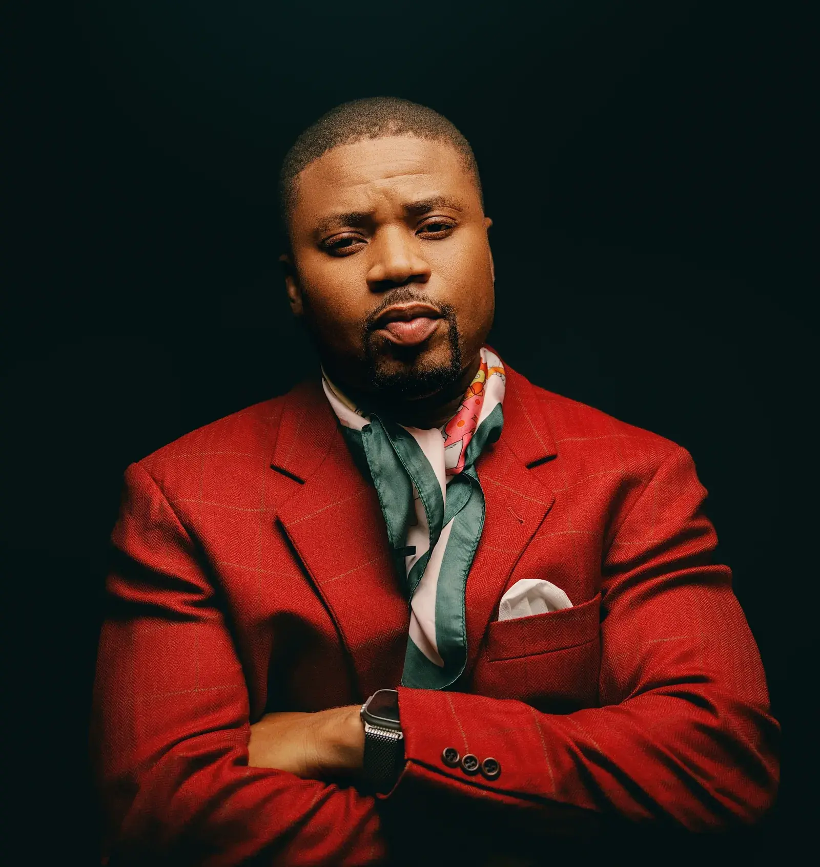 Ko'rale in a red suit and patterned tie against a deep teal backdrop